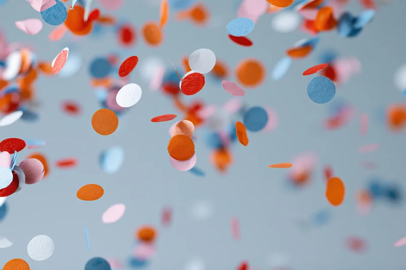 Colorful paper confetti pieces floating and falling midair against a gray background