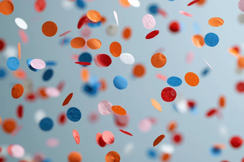 Colorful paper confetti pieces floating and falling midair against a light blue background