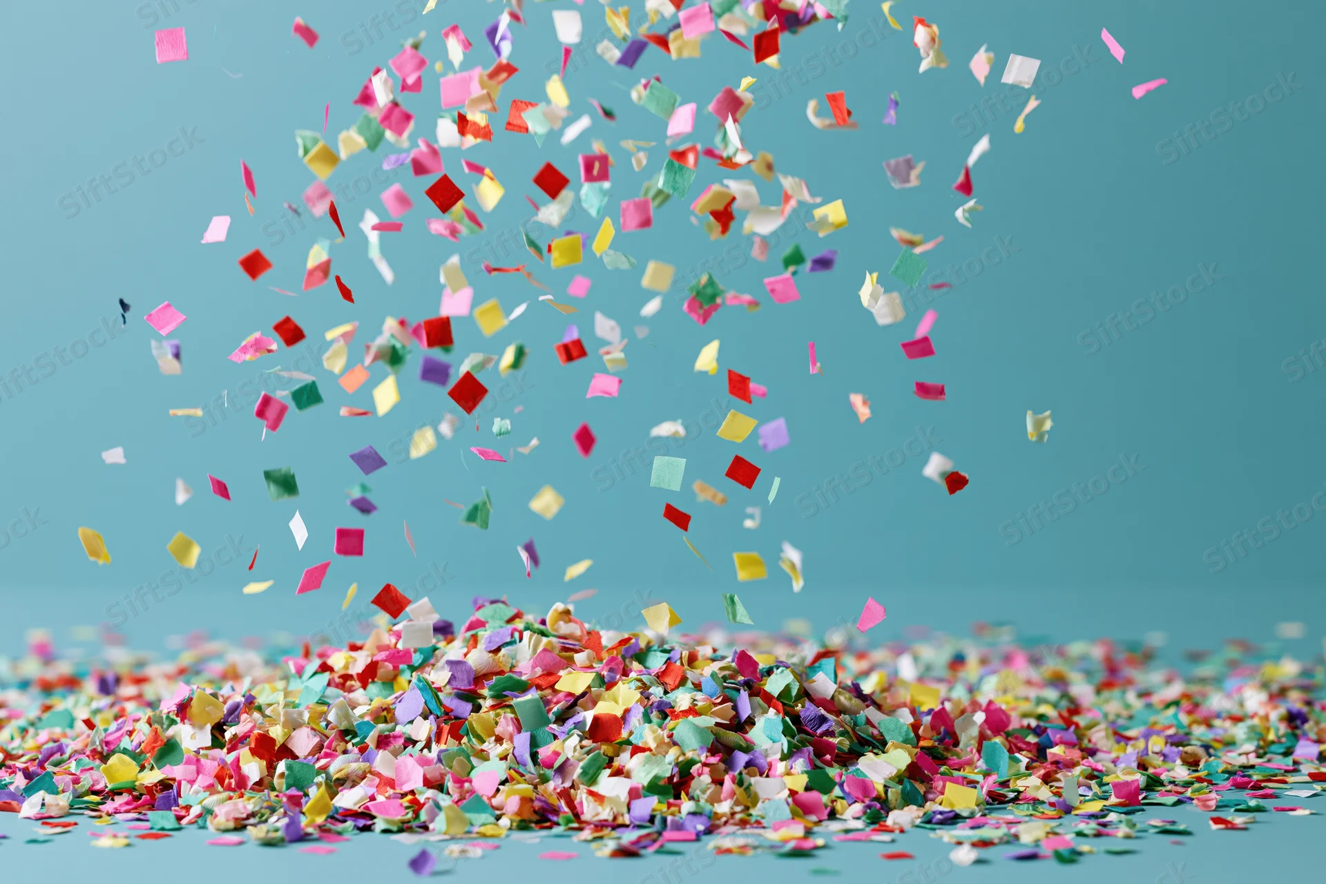 Colorful paper confetti falling and piling on a turquoise surface