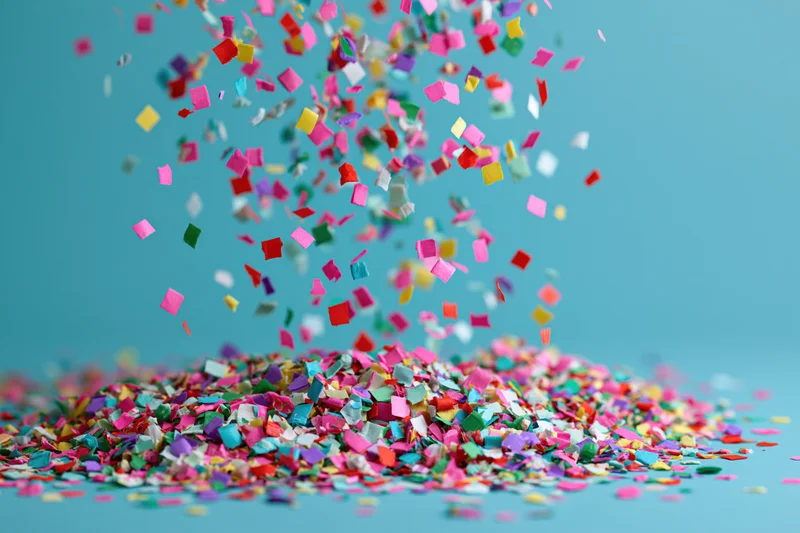Colorful paper confetti falling and piling up on a flat turquoise surface