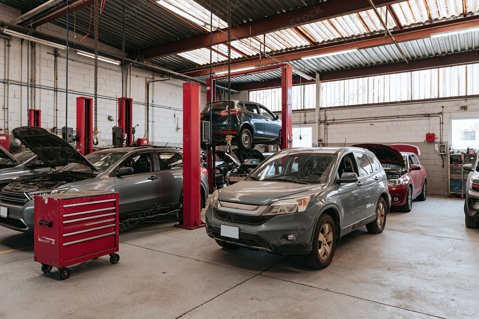 Multiple cars in various stages of repair inside an auto shop with lifts and tools visible