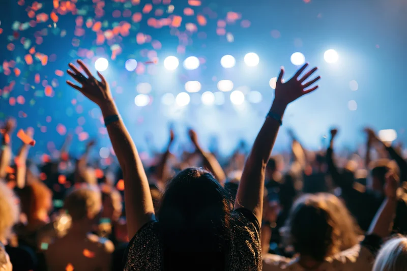 Crowd at concert with arms raised under stage lights and falling confetti