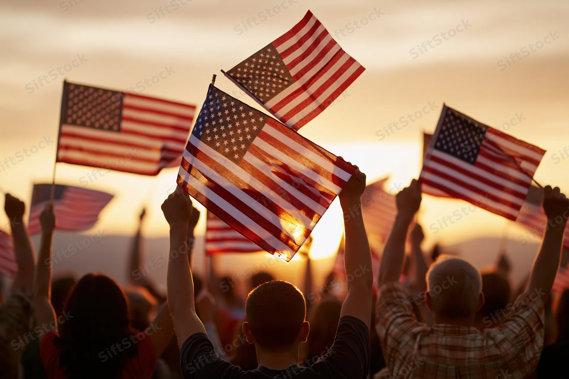 Crowd of people silhouetted from behind raising american flags at sunset