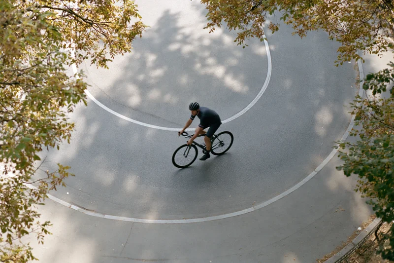 Cyclist riding a road bike along a curved asphalt path surrounded by autumn trees