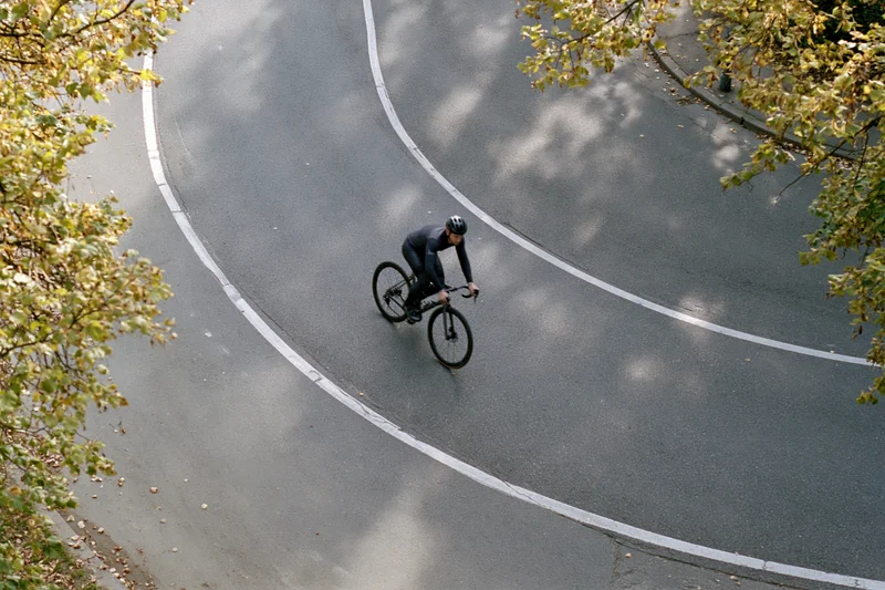 Cyclist riding a road bike along a curved asphalt path framed by autumn trees