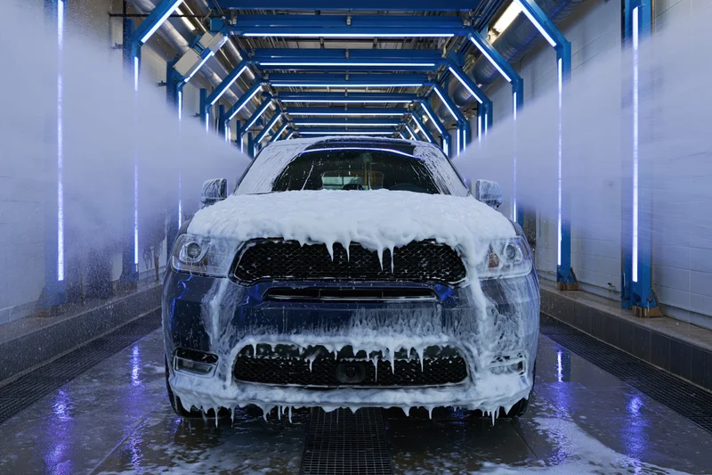 Dark suv covered in foam moving through automated car wash tunnel
