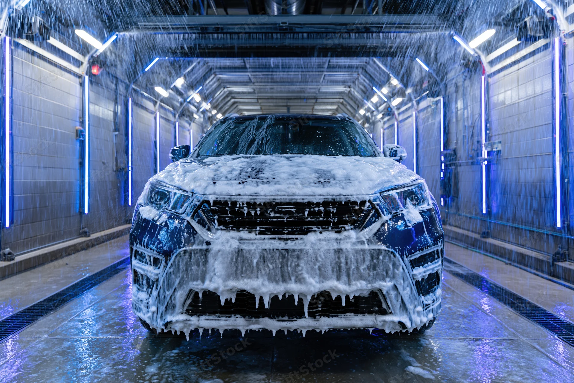 Dark suv covered in foam moving through automated car wash tunnel