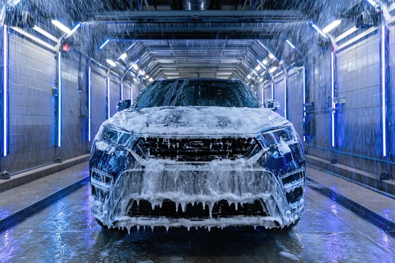 Dark suv covered in foam moving through automated car wash tunnel