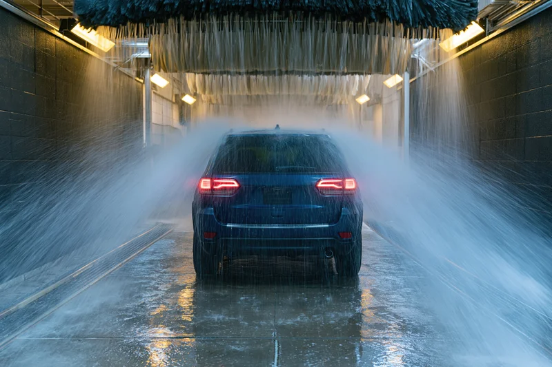 Dark blue suv moving through automated car wash tunnel with water spraying from overhead brushes