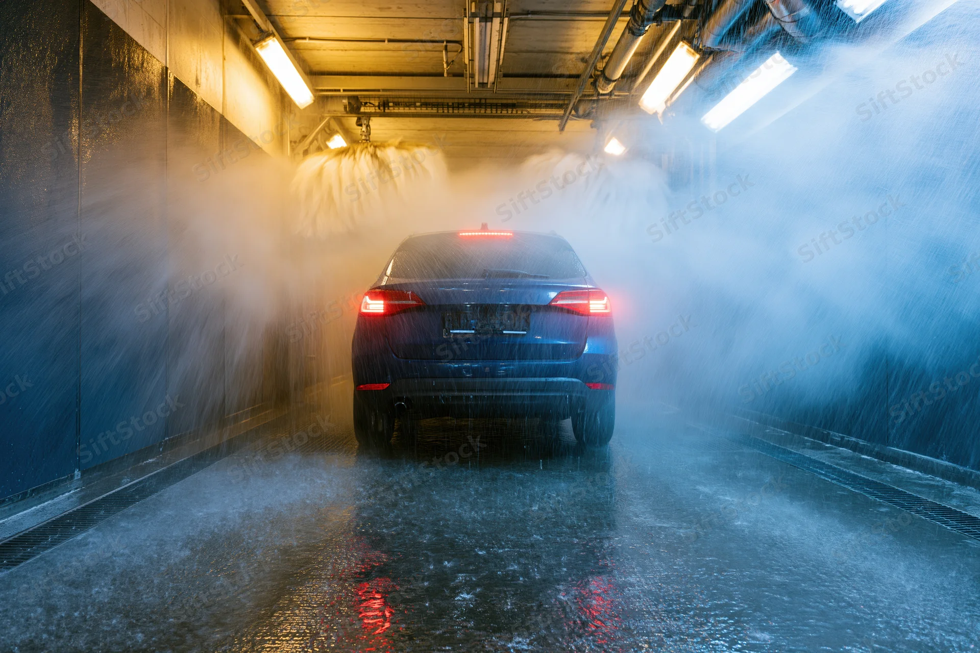 Dark blue suv moving through automated car wash tunnel with water spraying from above and sides
