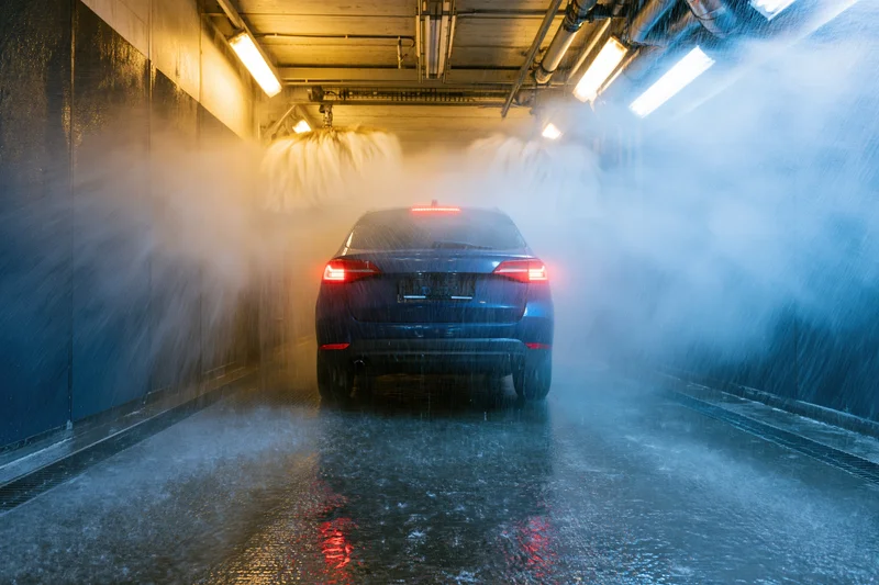 Dark blue suv moving through automated car wash tunnel with water spraying from above and sides