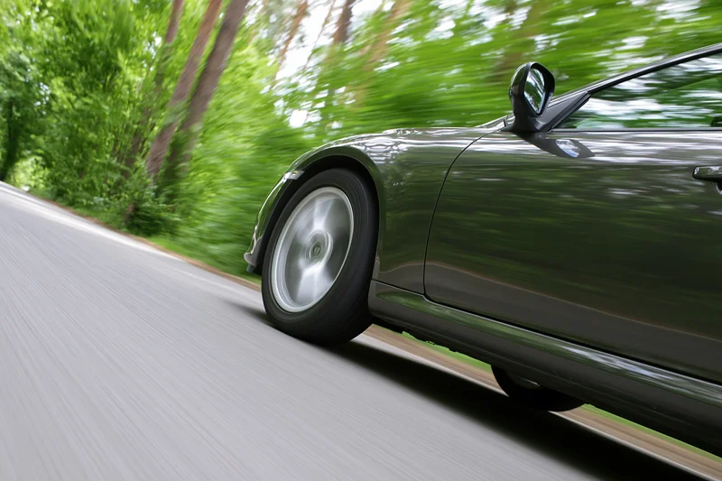 Dark metallic sports car accelerating along a tree-lined road