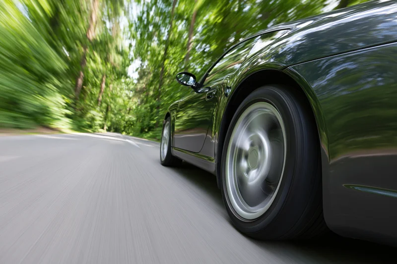 Dark metallic sports car accelerating on tree-lined road