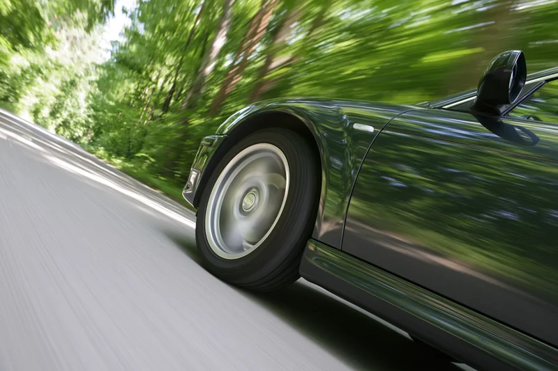 Dark metallic sports car accelerating along tree-lined road