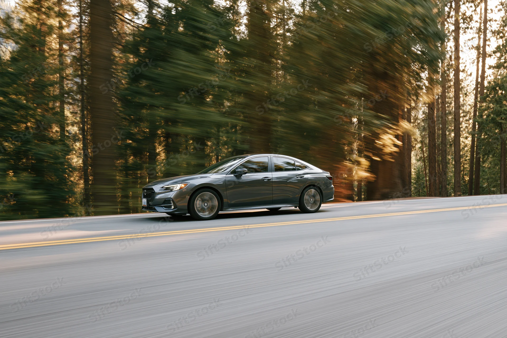 Dark silver sedan driving fast on a two-lane forest road with blurred trees and asphalt