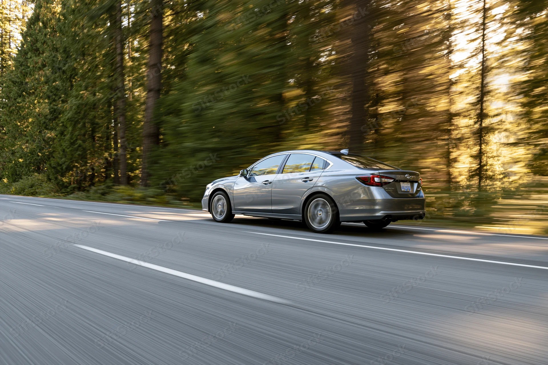 Silver sedan driving fast on a forest road with blurred trees and sunlight