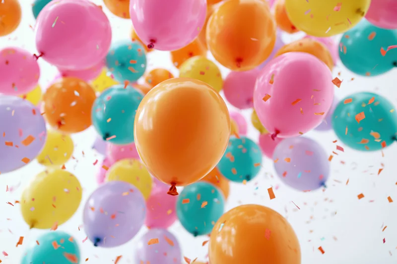 Colorful latex balloons floating upward with confetti against white background