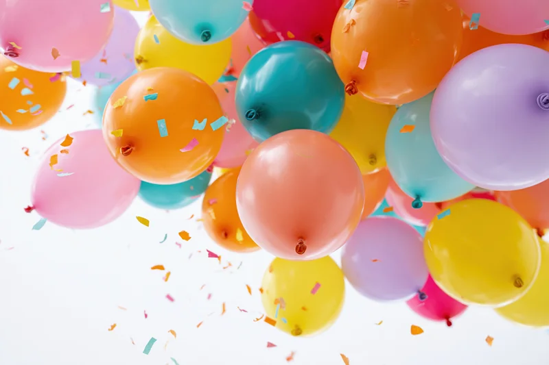 Colorful latex balloons floating upward with confetti against white background
