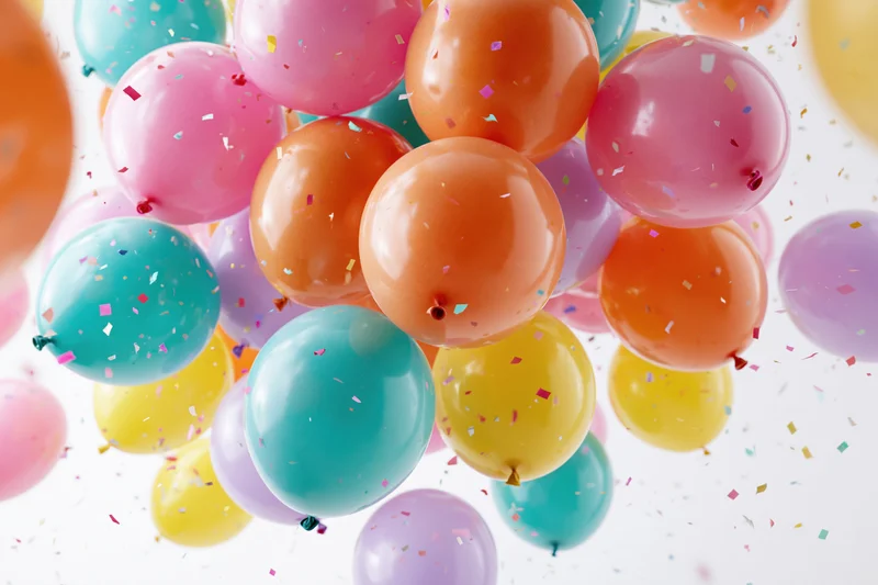 Colorful latex balloons floating upward with confetti against a white background