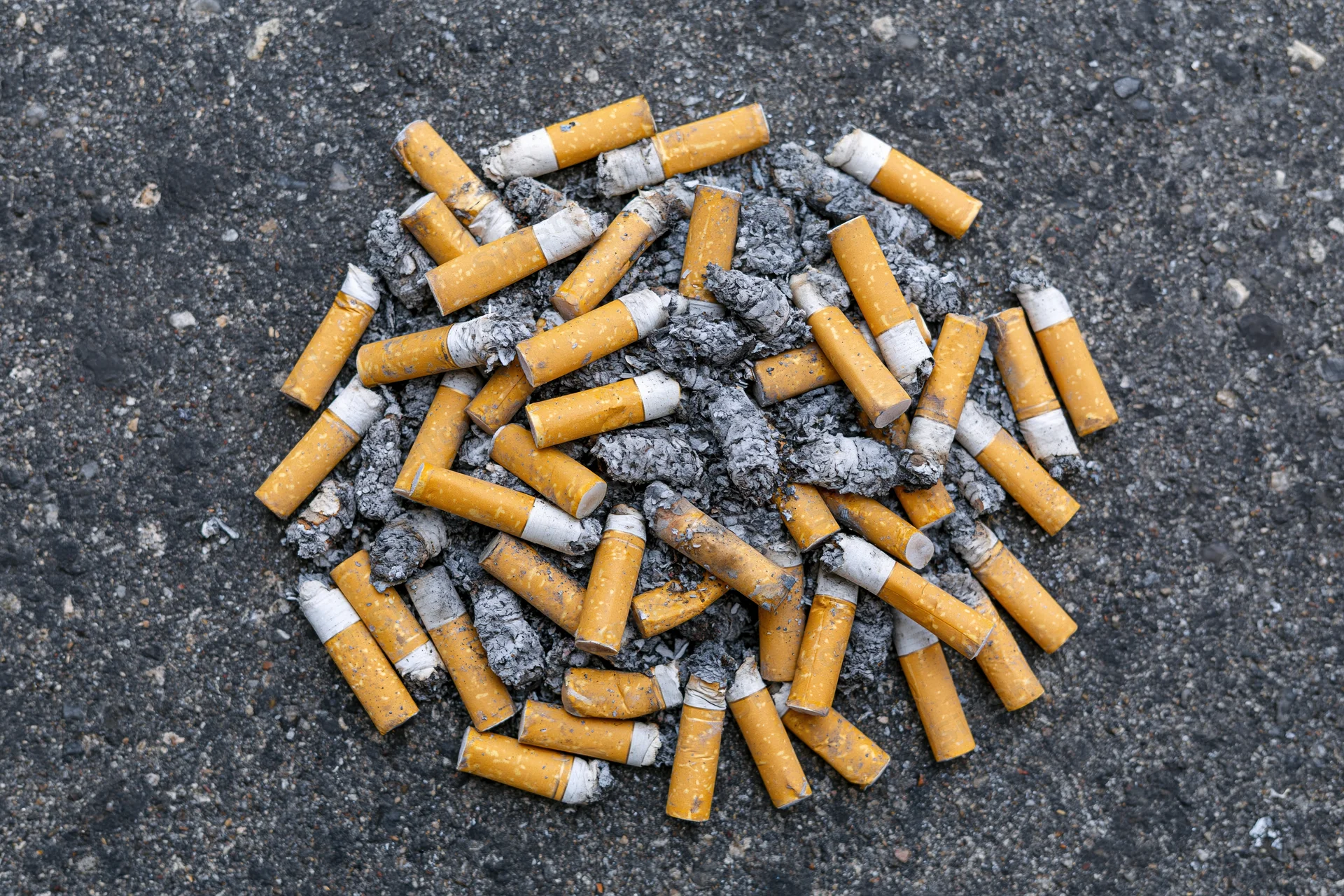 Cigarette butts and ash scattered on asphalt pavement
