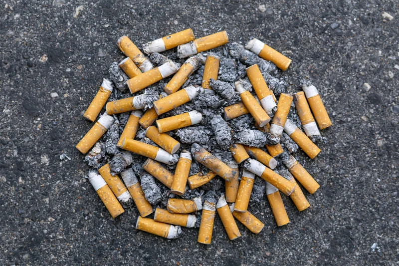 Cigarette butts and ash scattered on asphalt pavement