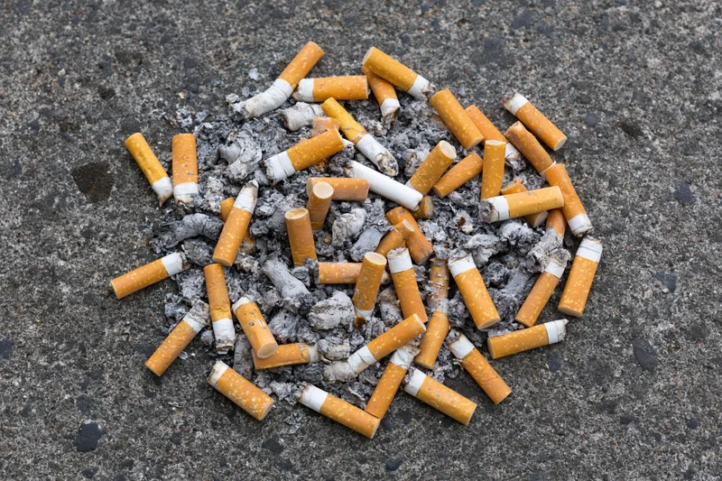 Cigarette butts and ash scattered on pavement surface