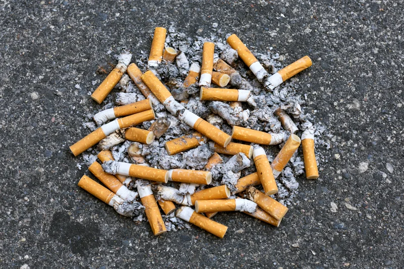 Cigarette butts and ash scattered on asphalt pavement
