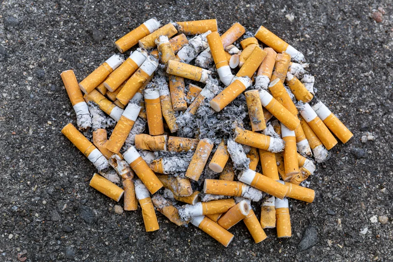 Cigarette butts and ash scattered on asphalt ground