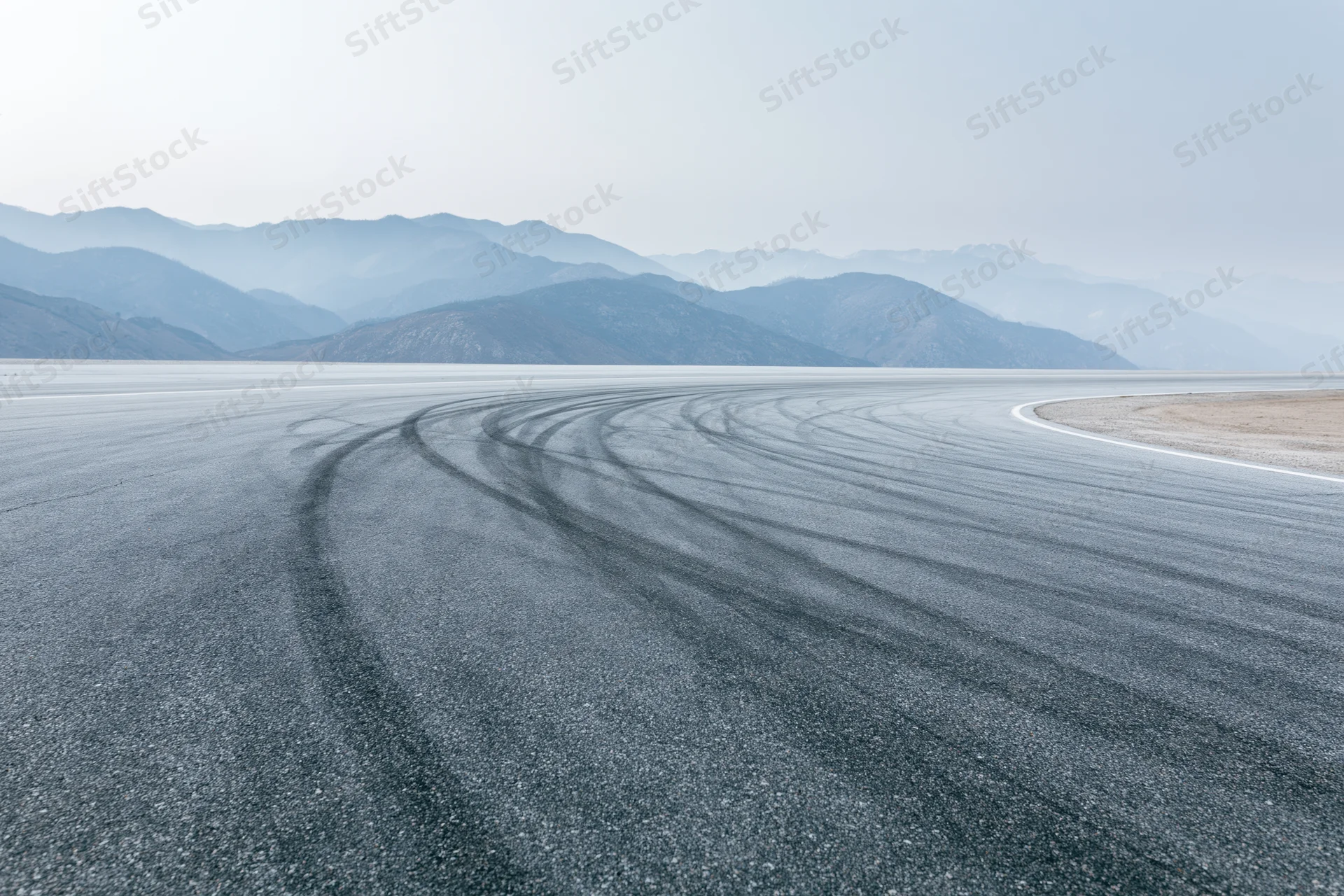 Curved asphalt racetrack with dark rubber burnout marks winding toward distant mountains