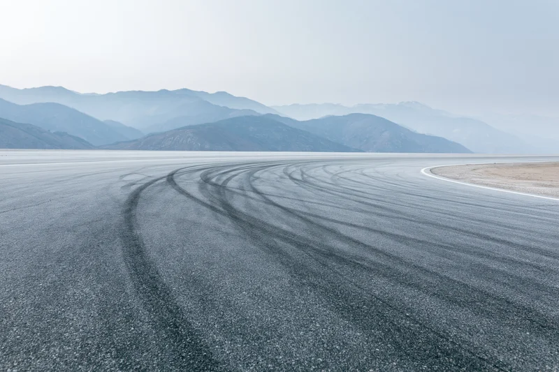 Curved asphalt racetrack with dark rubber burnout marks winding toward distant mountains