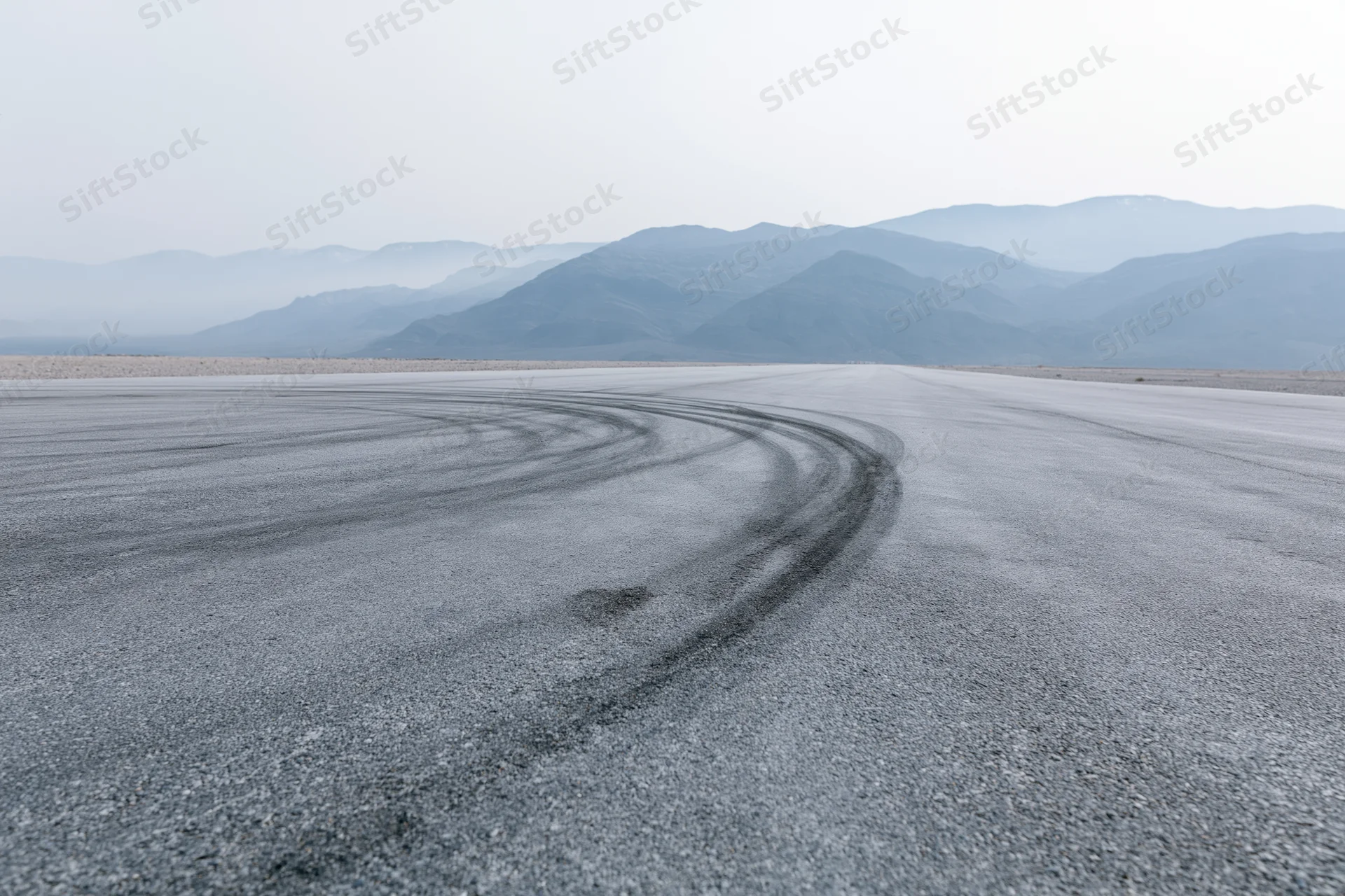 Curved asphalt racetrack with dark rubber burnout marks in a desert landscape