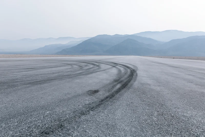 Curved asphalt racetrack with dark rubber burnout marks in a desert landscape