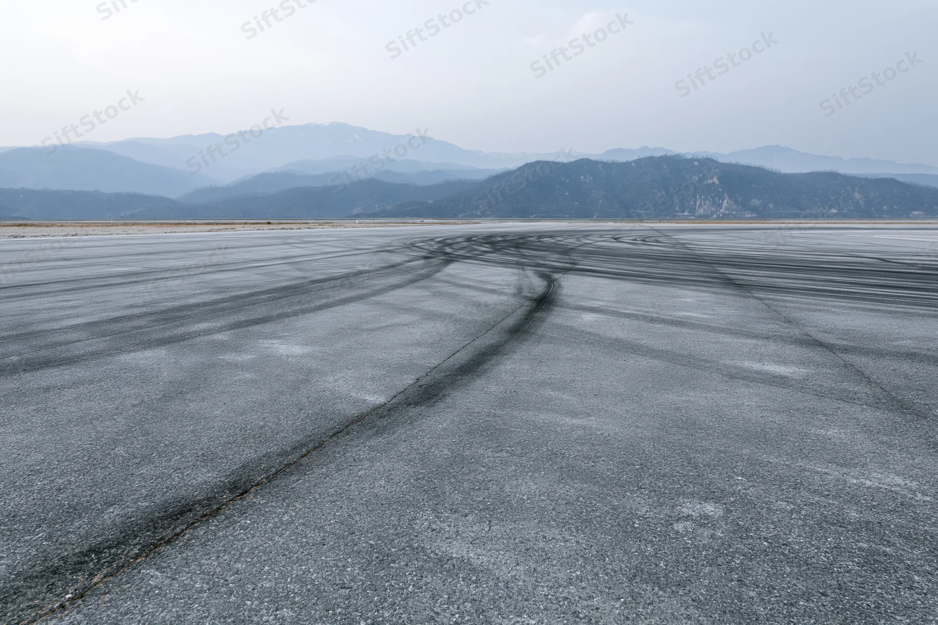 Empty asphalt racetrack with dark rubber burnout tire marks curving across the surface toward distant mountains