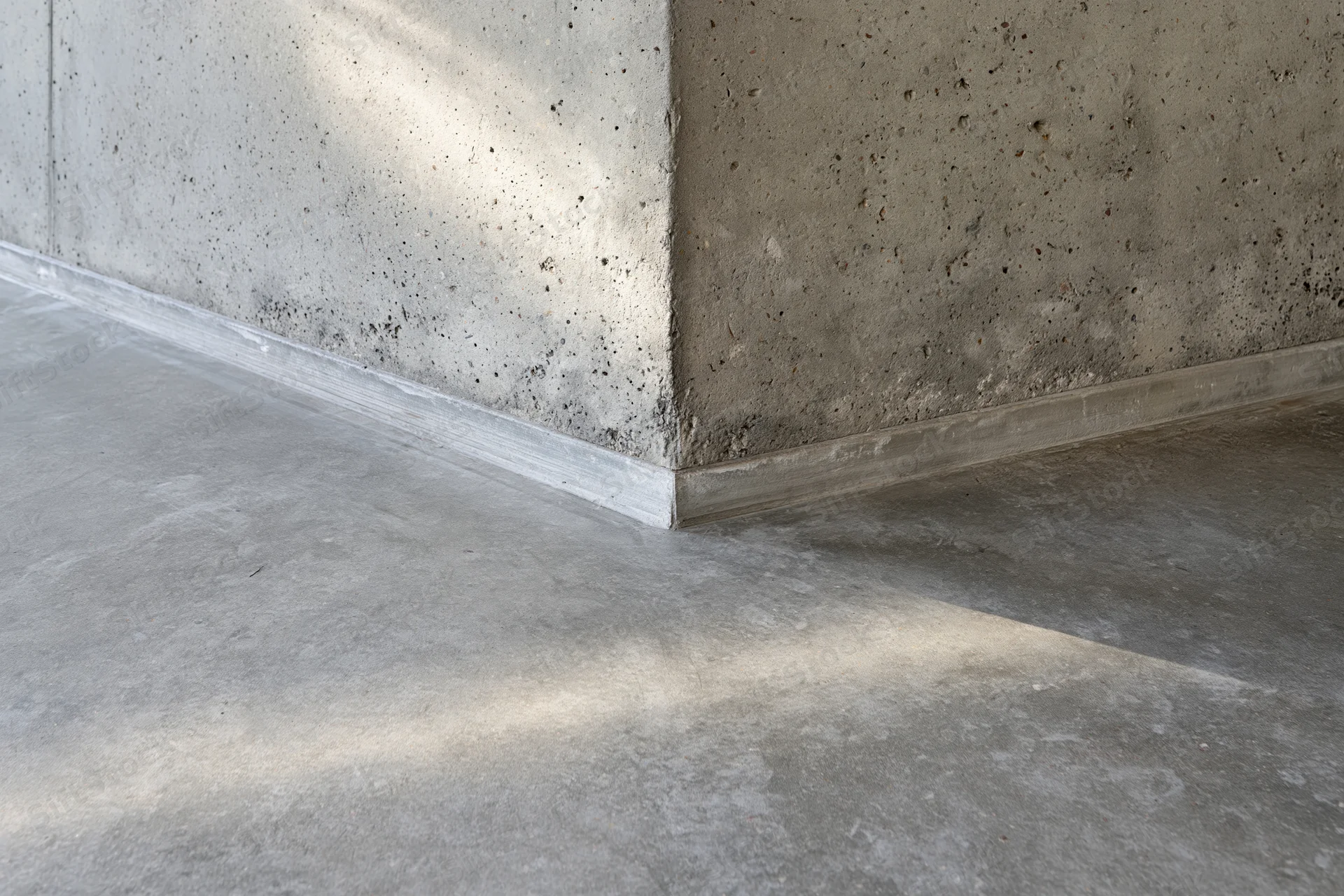 Corner of a concrete wall meeting a polished cement floor in an empty room interior