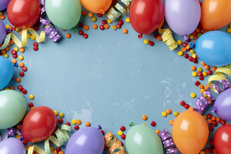 Colorful party balloons and streamers arranged in a frame around a blue surface with copyspace