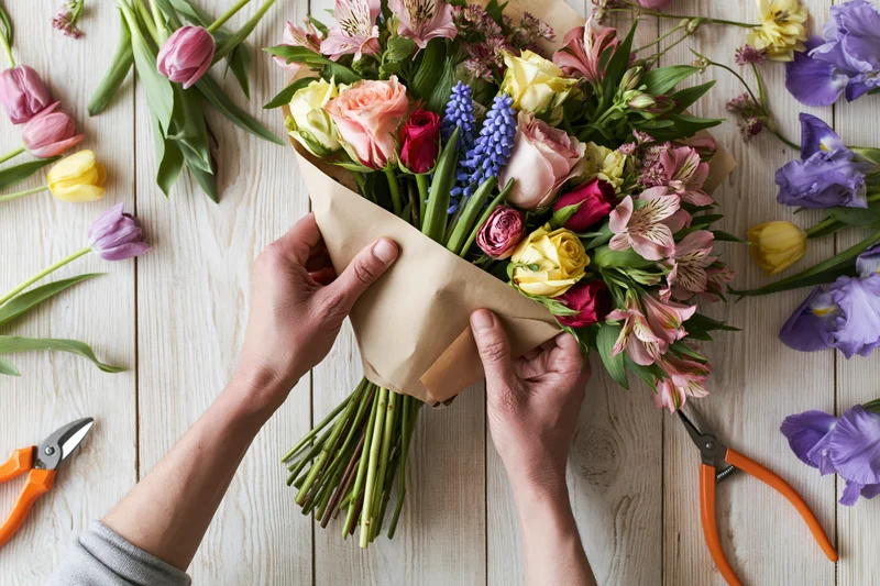 Florist hands wrapping a mixed bouquet of roses, hyacinths, tulips and irises on a wooden table