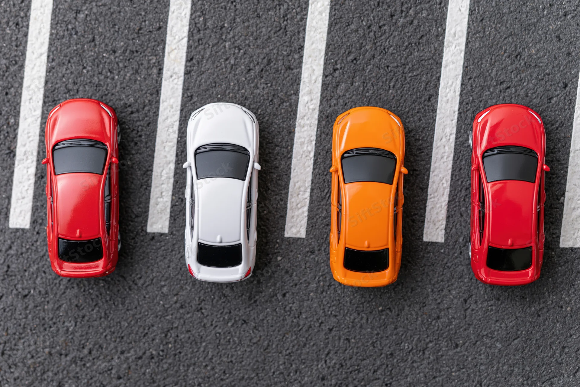 Four toy cars in a row parked in angled spaces on asphalt parking lot