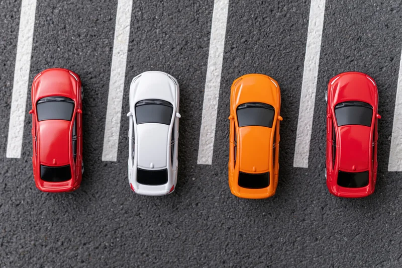 Four toy cars in a row parked in angled spaces on asphalt parking lot