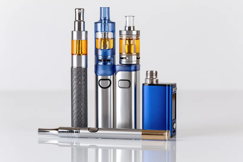 Five vaping devices arranged on a reflective white surface with one lying horizontally in front