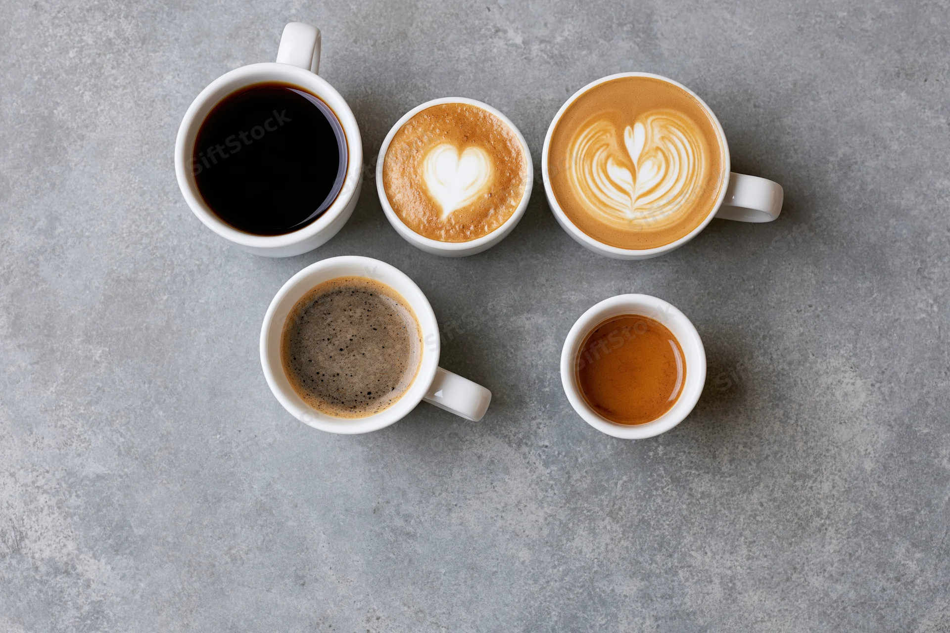 Five white ceramic coffee cups with different drinks and latte art arranged on a gray stone surface viewed from above