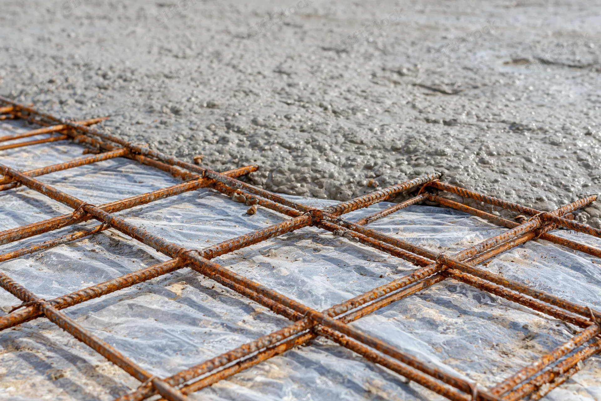 Wet concrete spreading over a steel rebar grid on a construction site