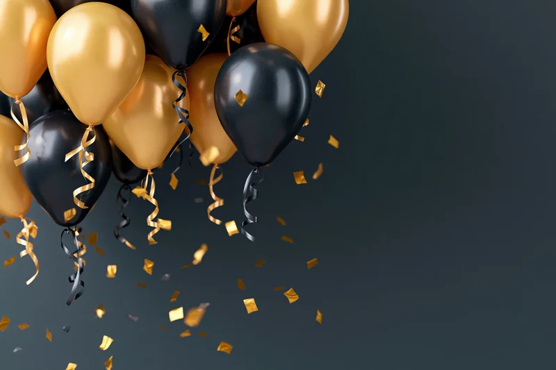 Gold and black helium balloons clustered in the upper left with falling confetti and streamers against a dark background, copyspace on the right