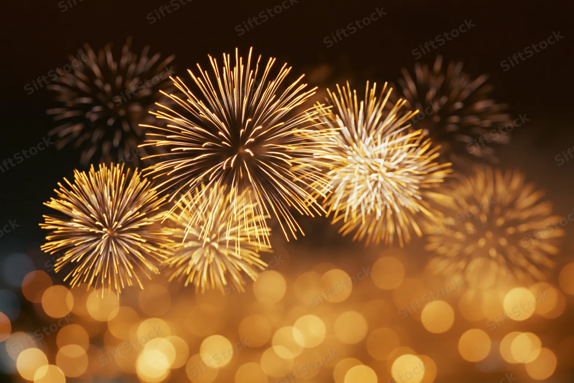 Golden and white fireworks bursting in the night sky over a bokeh-lit cityscape