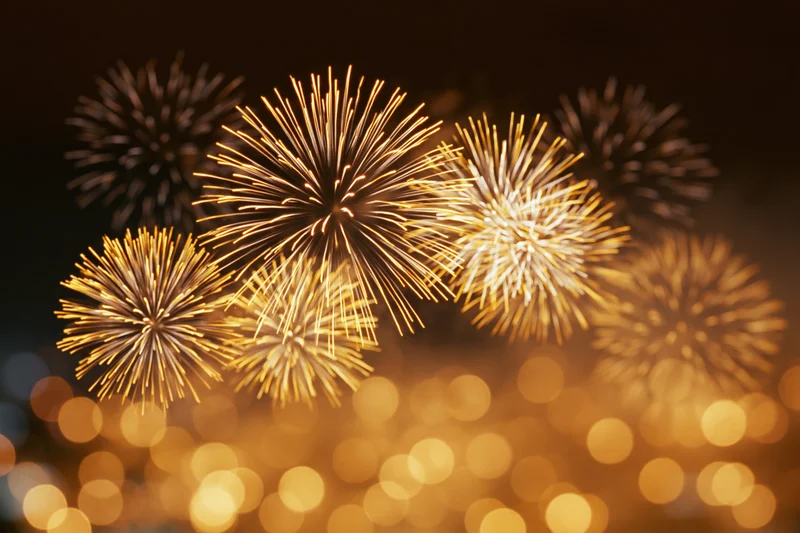 Golden and white fireworks bursting in the night sky over a bokeh-lit cityscape
