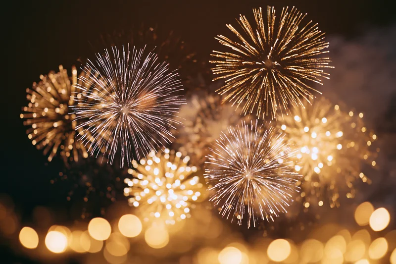 Golden and white fireworks bursting in the night sky with bokeh lights below