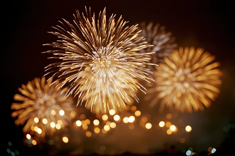 Golden and white fireworks bursting in the night sky over a cityscape with bokeh lights below