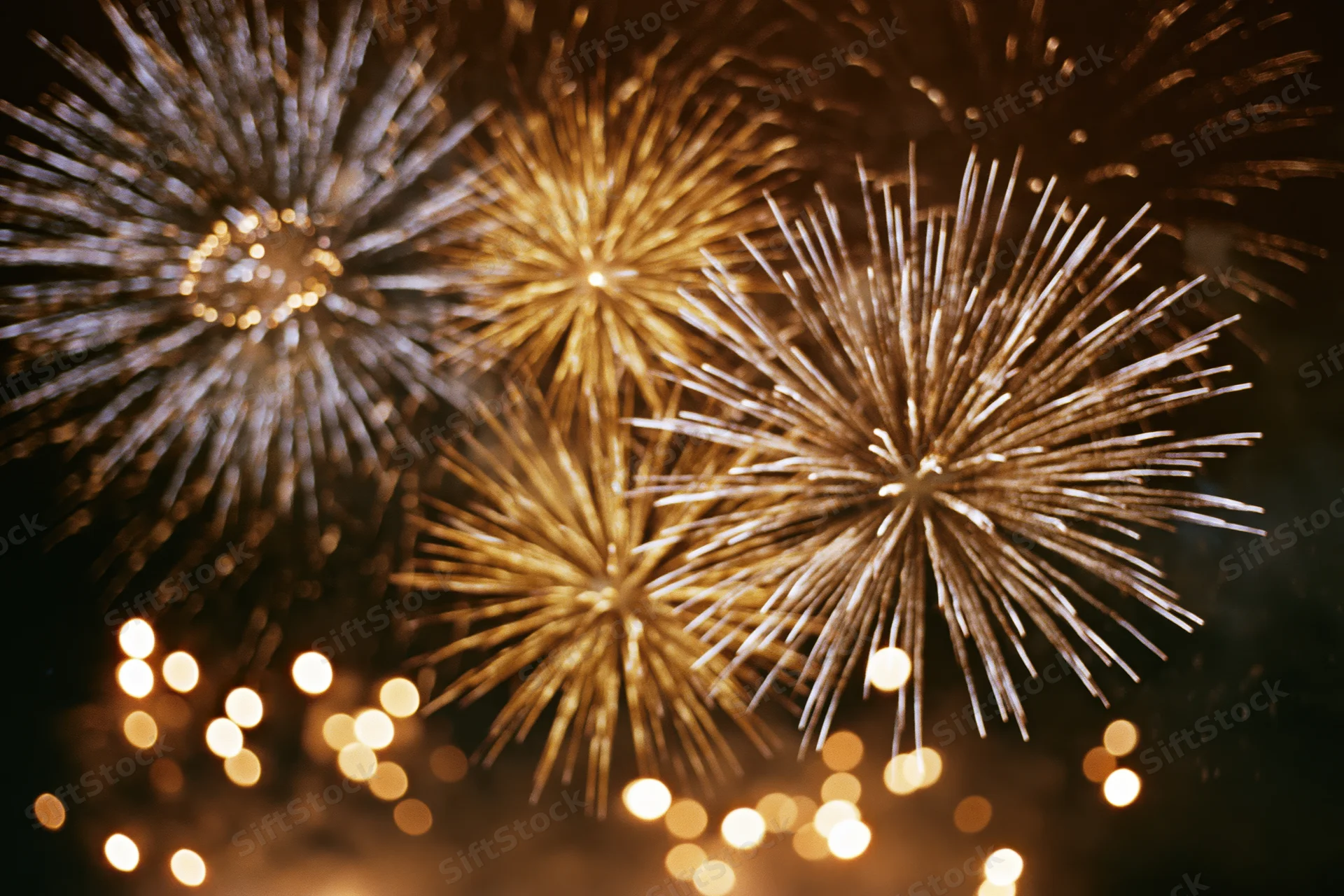 Golden and white fireworks bursting in the night sky with bokeh lights below