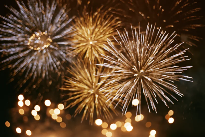 Golden and white fireworks bursting in the night sky with bokeh lights below