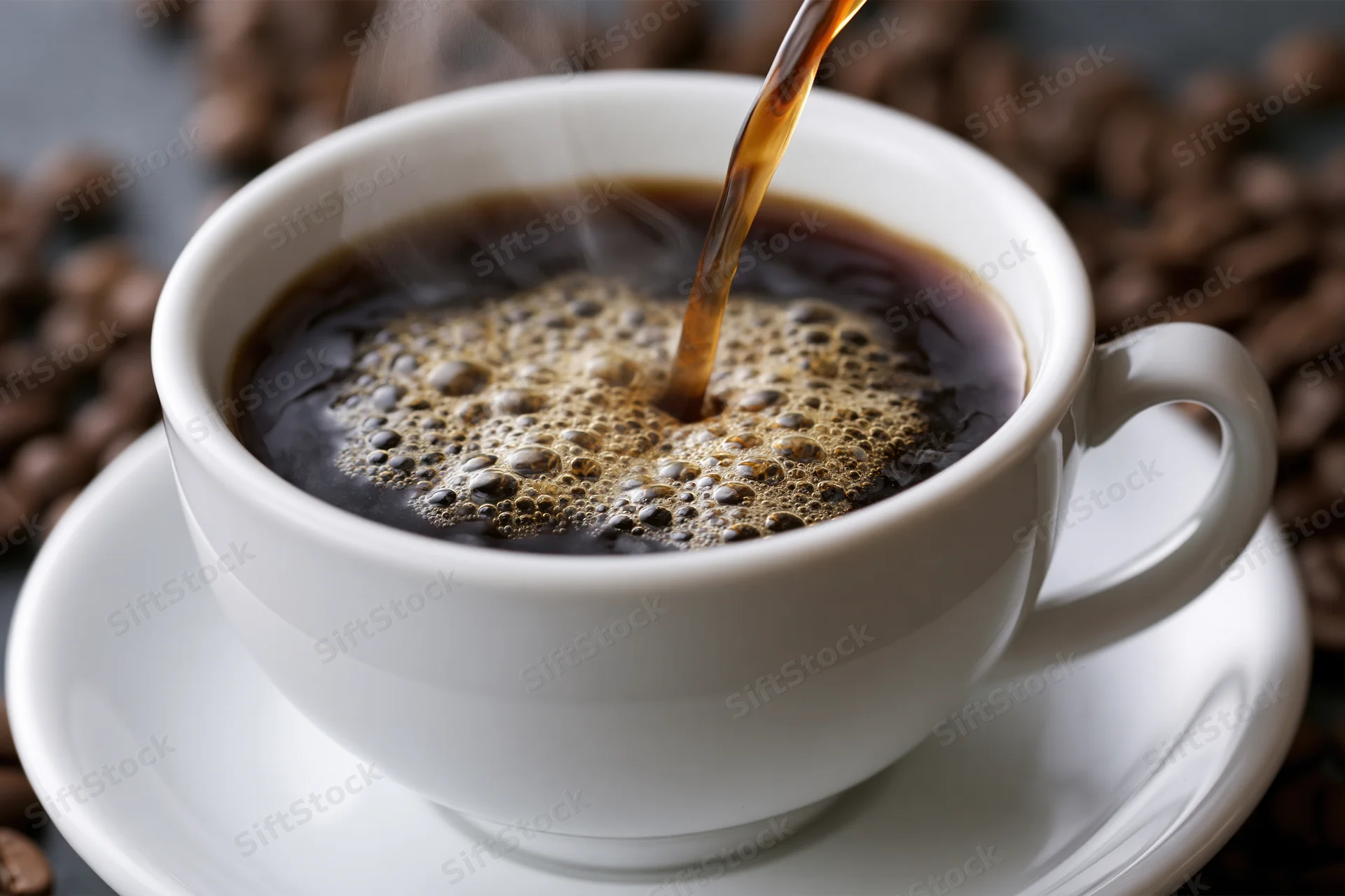 Hot black coffee being poured into a white ceramic cup on a saucer with coffee beans around