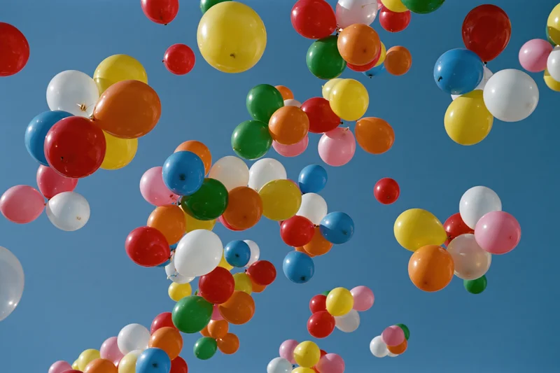 Multicolored balloons floating upward in the open sky during a celebration